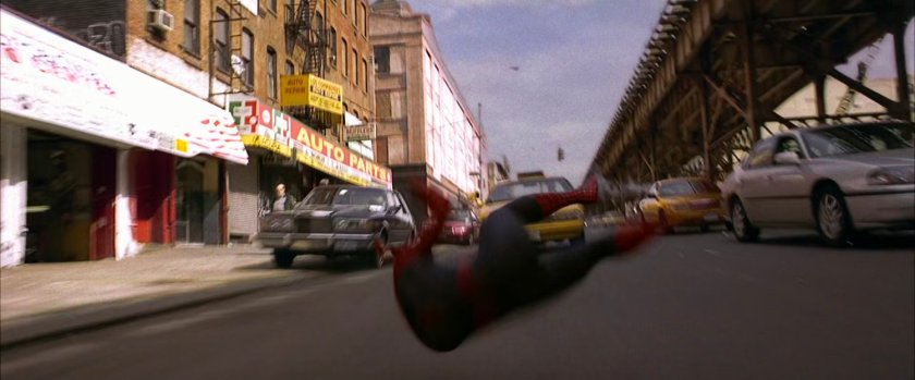 Spider-Man crashes into street next to elevated train tracks.