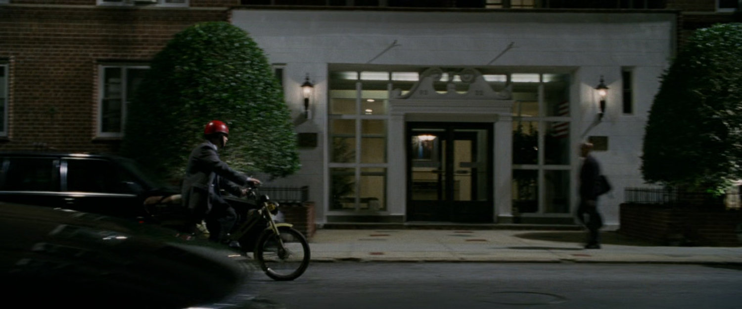 Peter Parker on Moped at night in front of Aunt May's apartment building.