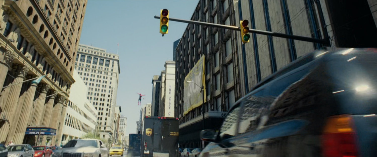 Spider-Man leaps over truck on city street.