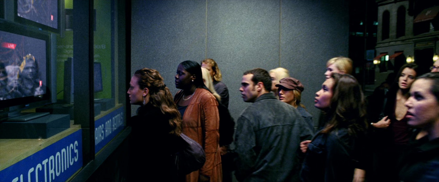 People standing outside a store watching television through the window.