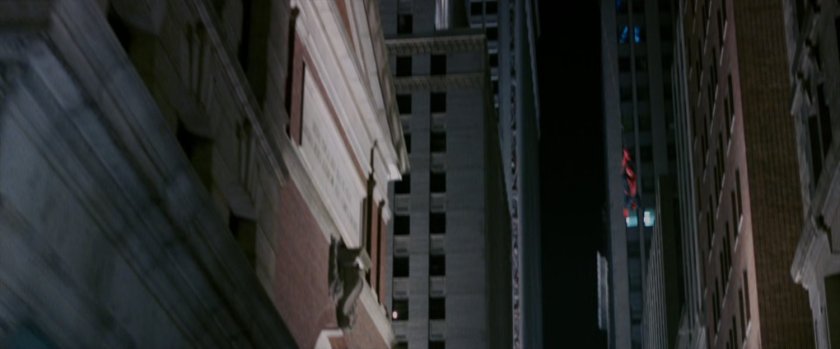 Spider-Man swings through a street at night.