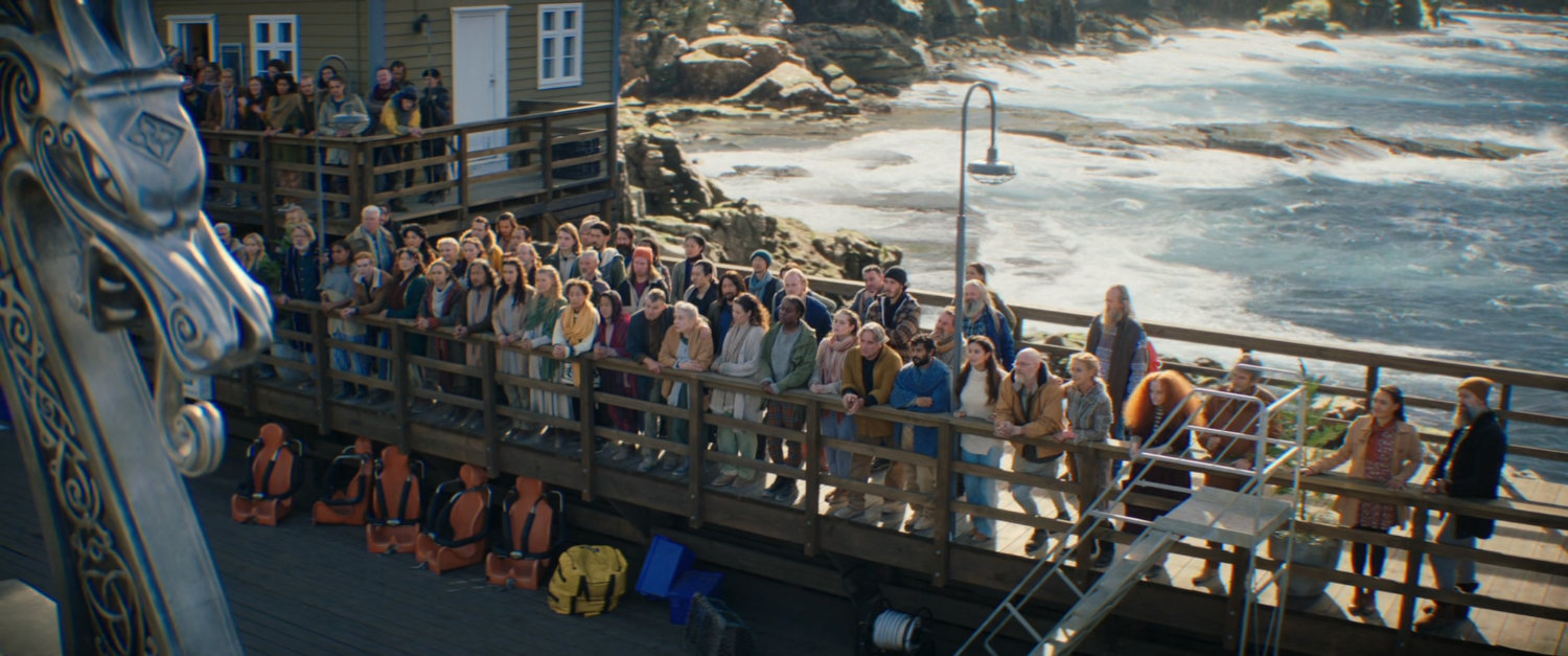Townsfolk of New Asgard stand on a pier and wait for the dragon boat to leave.