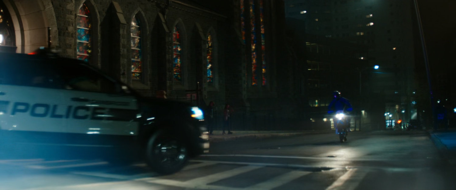 Police car chasing motorcycle in front of church at night.