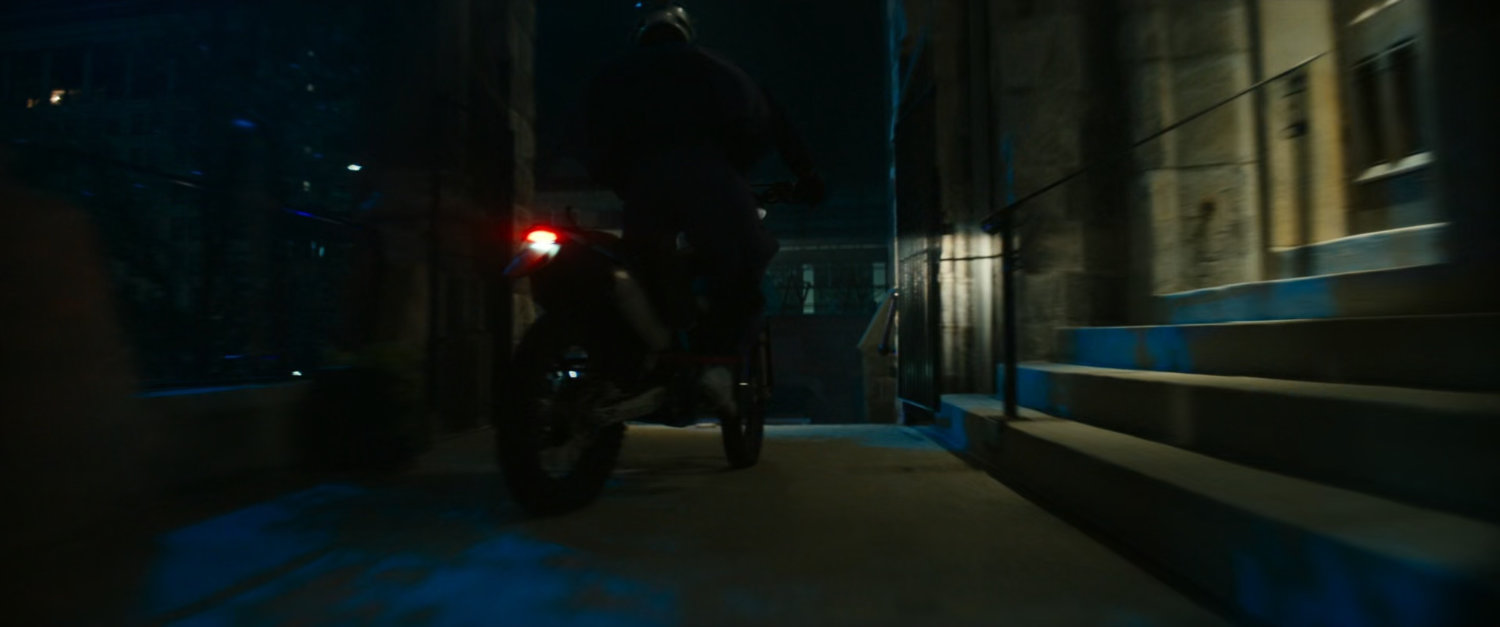 Motorcycle driving on church sidewalk at night.