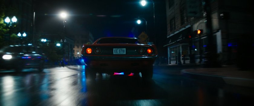 Red car driving on Boston street at night.