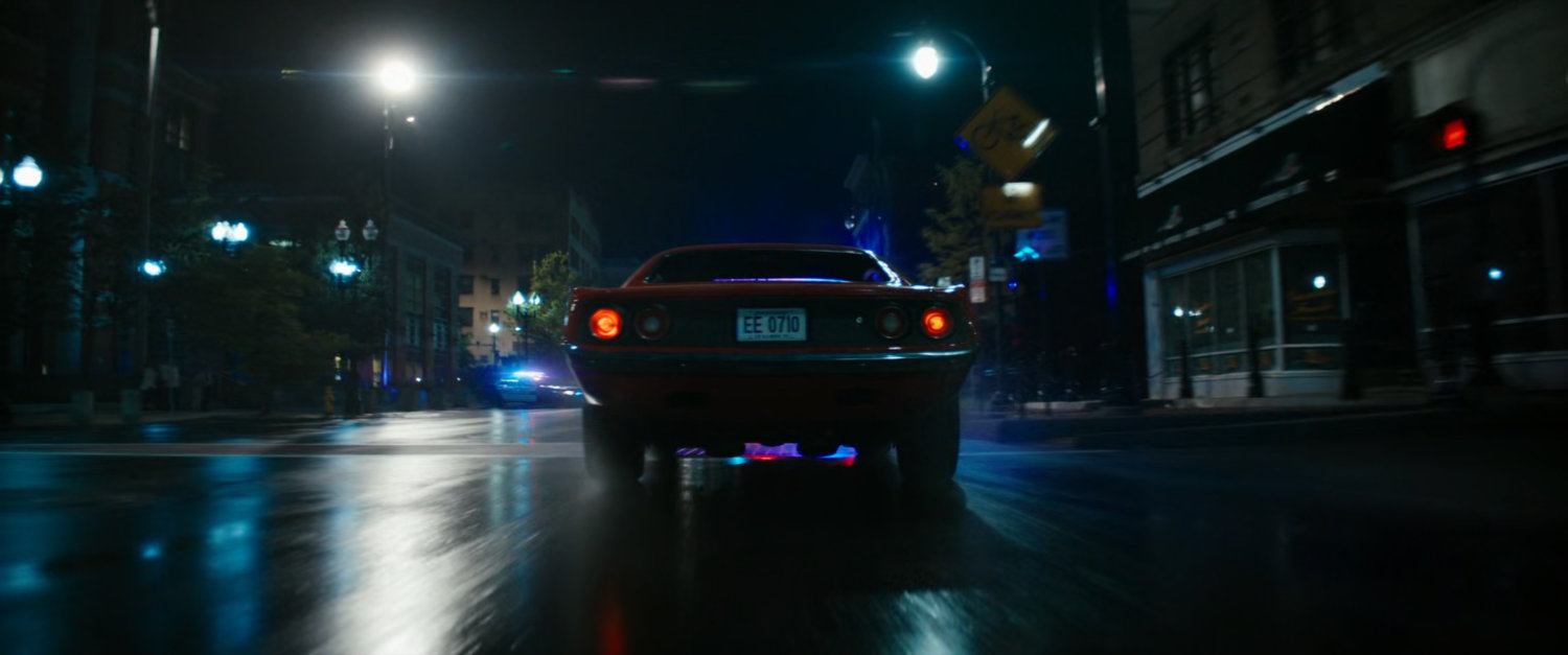 Red car driving on Boston street at night.