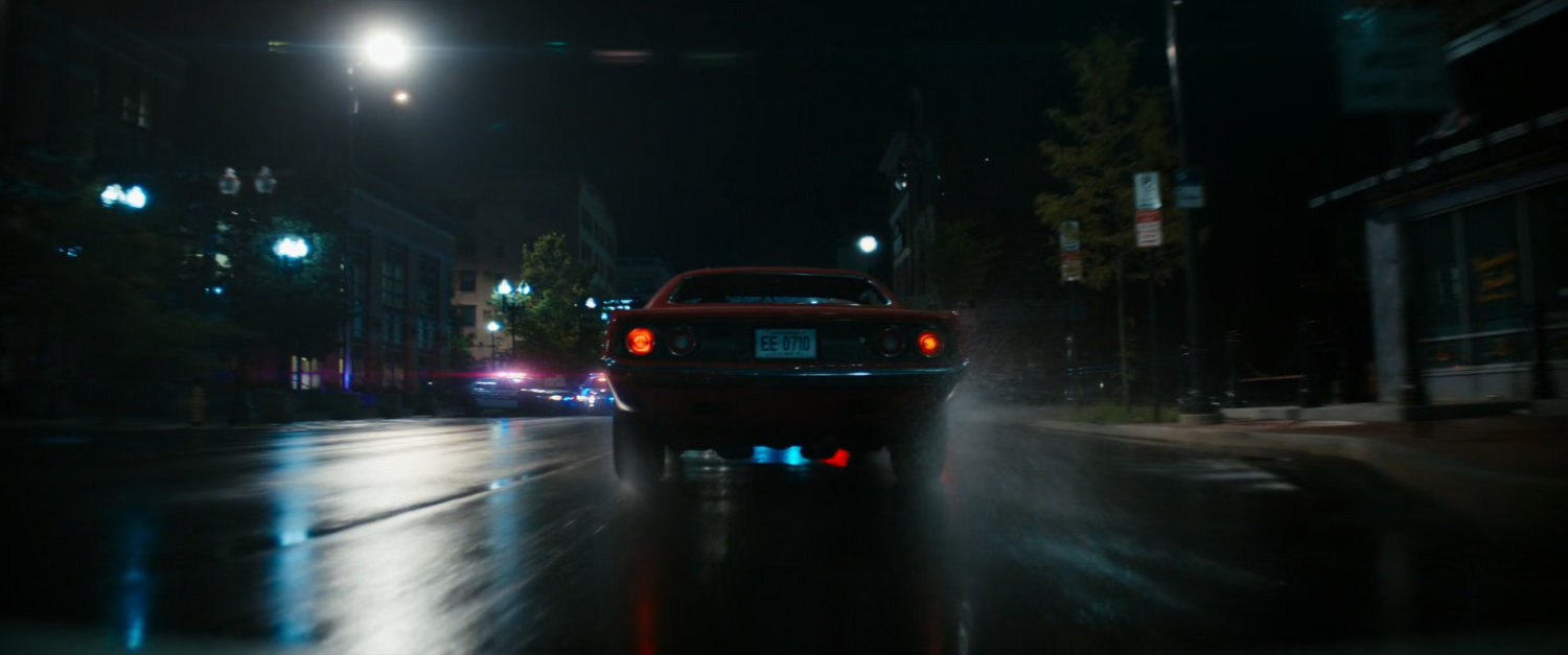 Red car driving on Boston street at night.