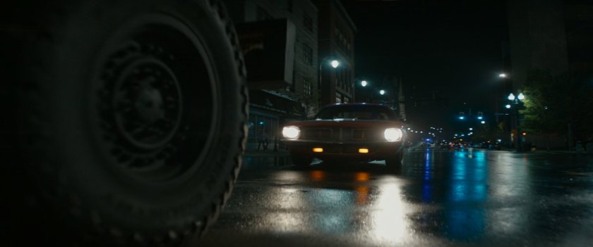 Red car driving on Boston street at night.