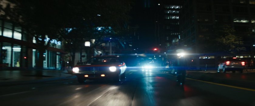 Red car and motorcycle driving on Boston street at night.