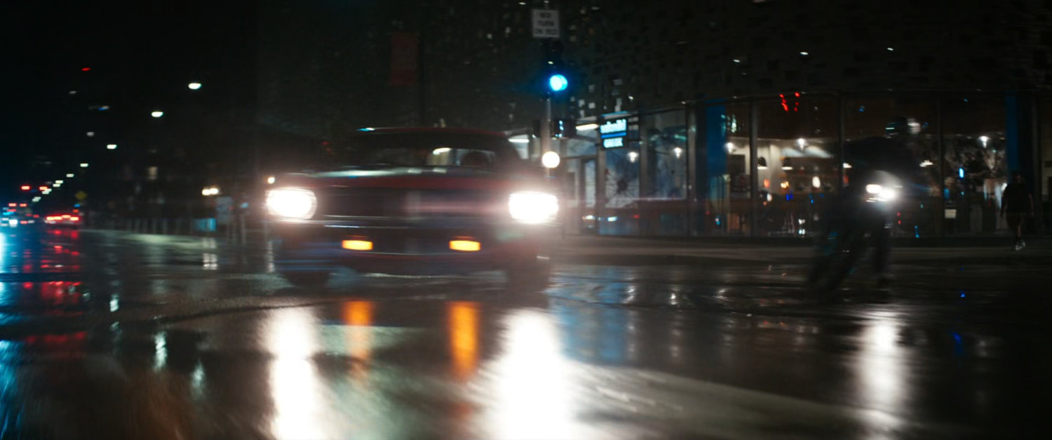 Red car and motorcycle cornering on Boston street at night.