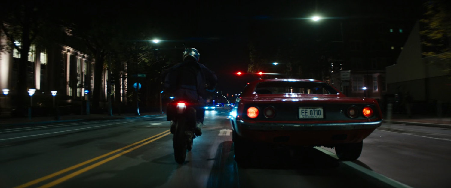 Red car and motorcycle driving on Boston street at night.