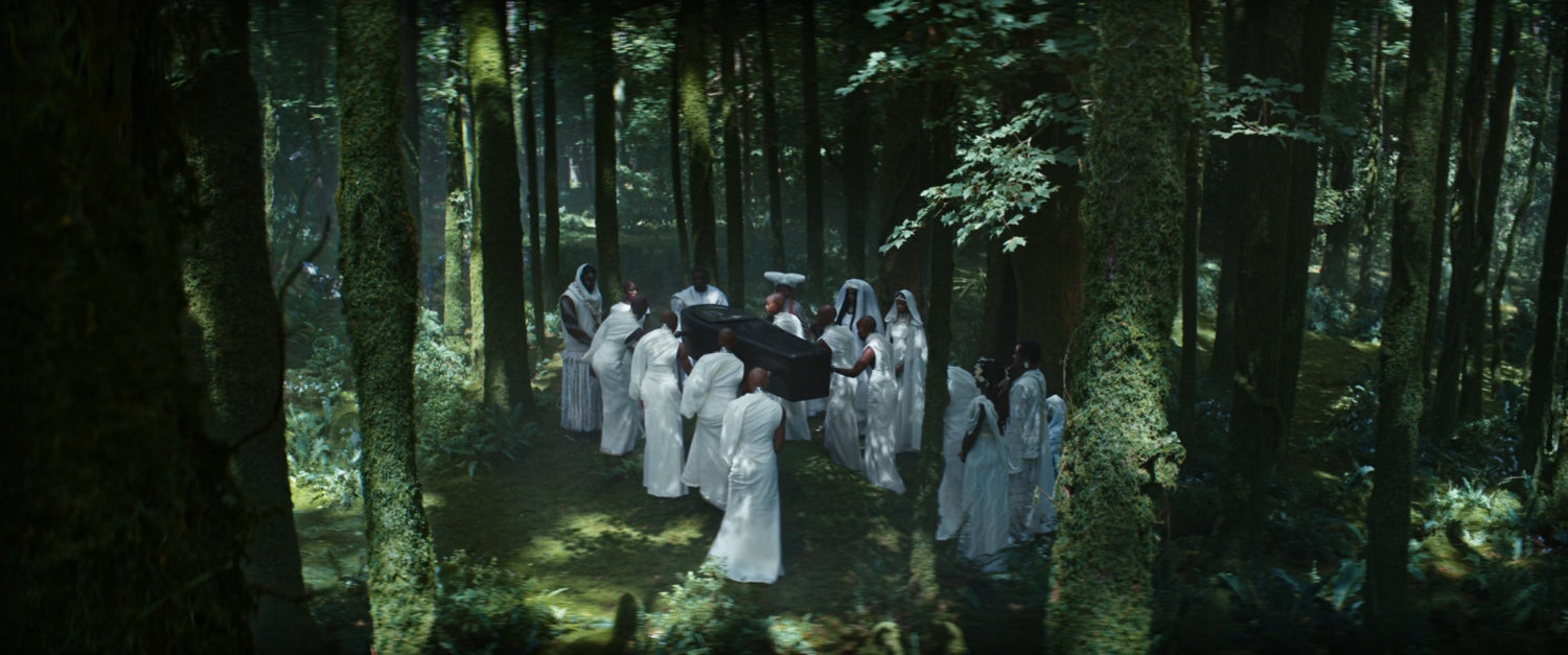 Wakandans wearing white carry a coffin though the woods.