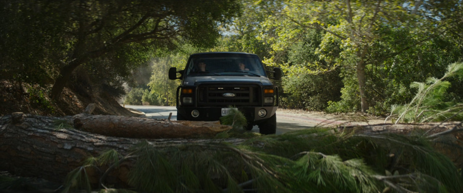 Van stopping on road in front of felled tree.