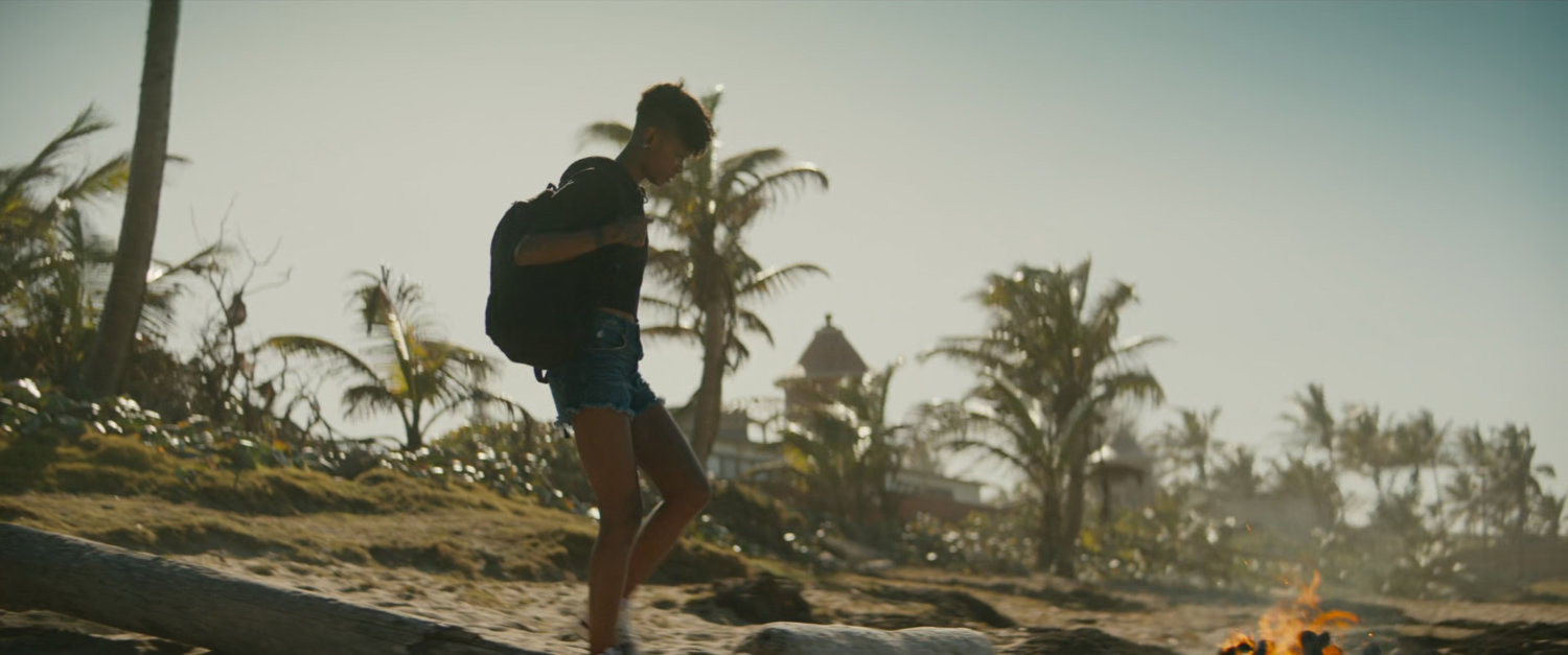 Shuri walks towards a campfire on a beach.