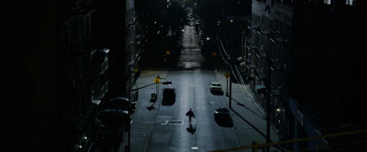 A lone figure runs down a dark New York street at night.