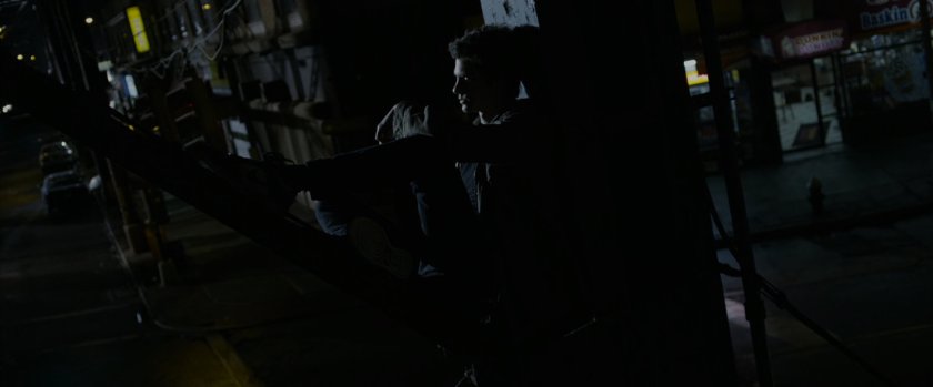 Peter Parker sits on the beams of a bridge at night.
