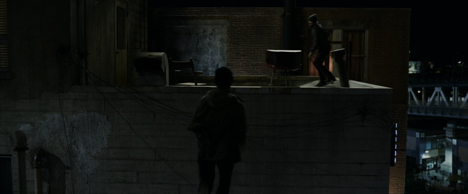 Peter Parker chases a thug across the roof at night.