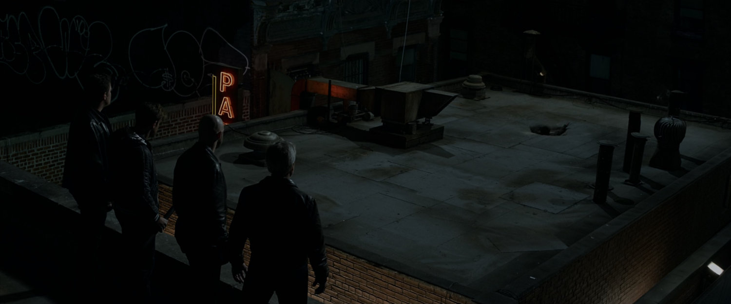 Thugs watch as Peter Parker falls through a roof at night.