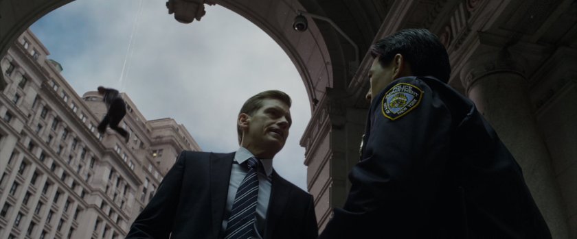 Captain Stacy and police officer chat while a thug is suspended behind them on a web.