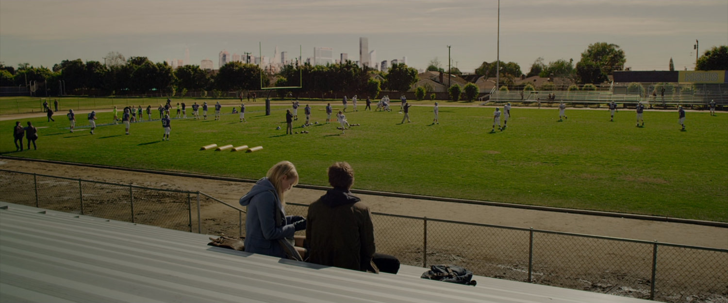 Gwen and Peter Parker on the bleachers at a high school stadium.