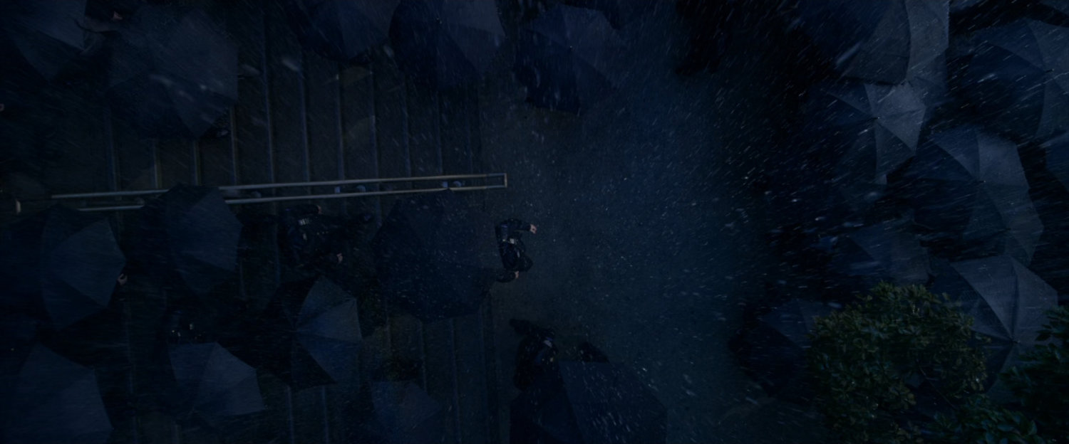 POV from roof of mourners with umbrellas outside church.