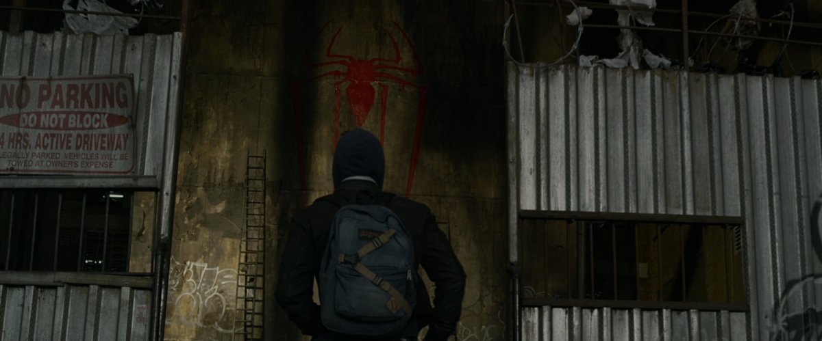 Peter Parker looking into alley where Spider-Man log has been spray painted.