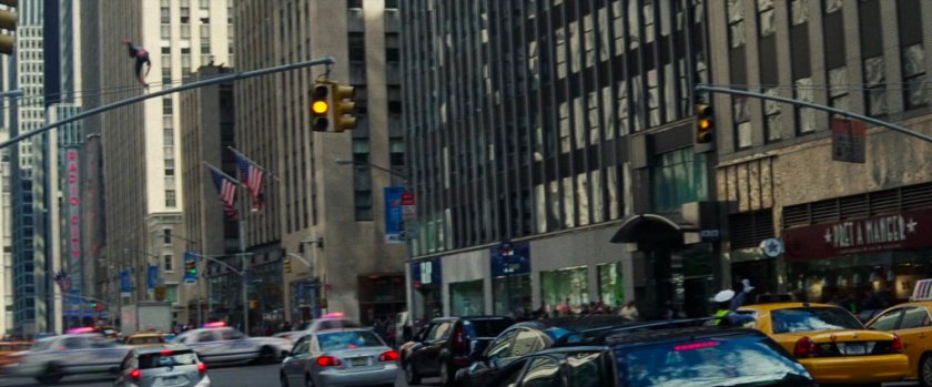Spider-Man swings past a crowded New York City street.