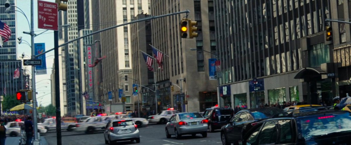 Spider-Man swings past a crowded New York City street following police cars.