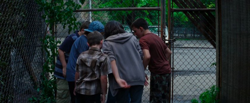 Older boys bully younger child by chain link fence.