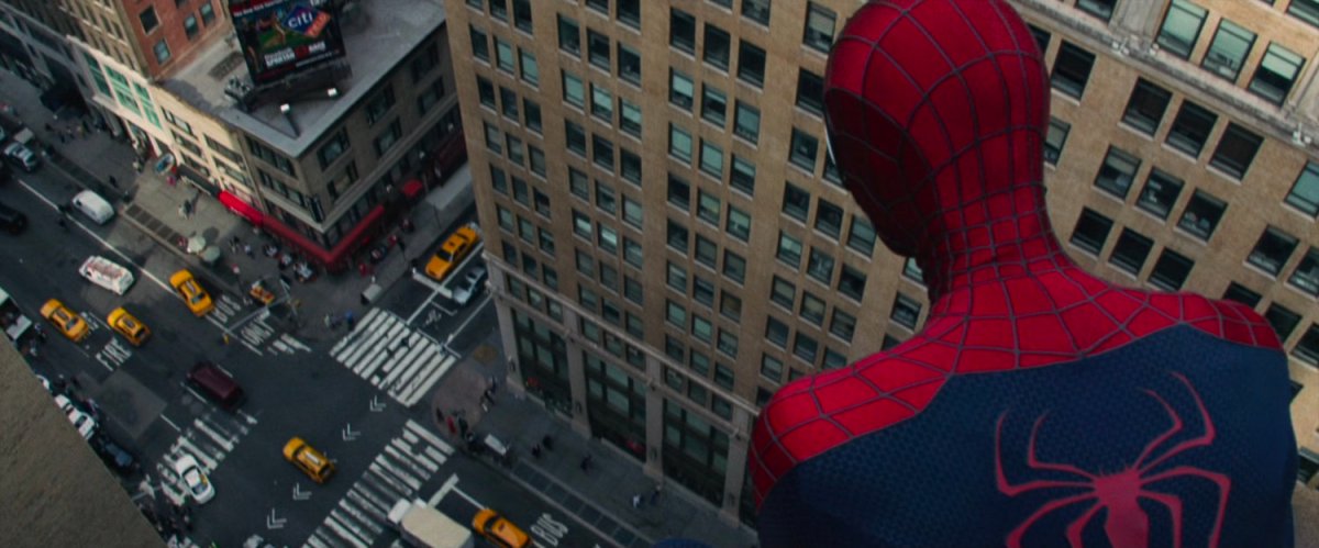 Spider-Man looks down at an intersection from atop a building.