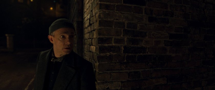 Agent Ross peering around a corner of a brick building.