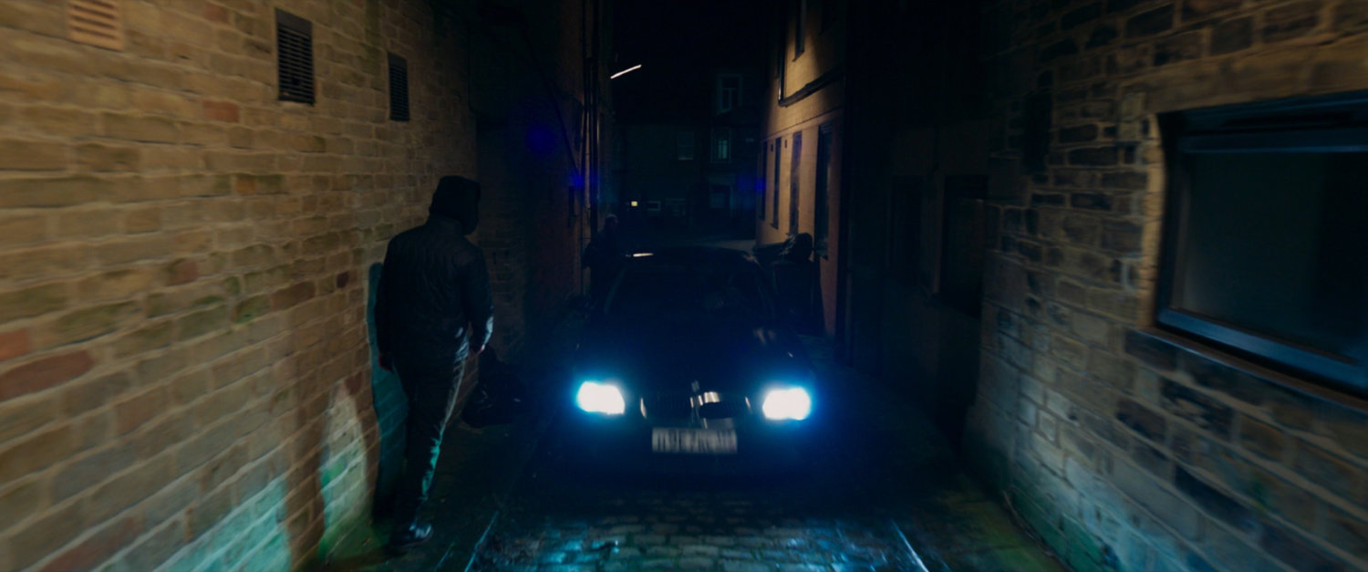 A car driving towards camera in a dark narrow alley.