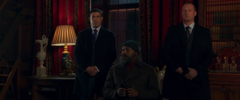 Nick Fury seated by two MI6 Agents in an ornate study.