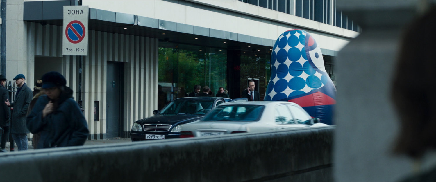 G'iah POV of car parked in front of Moscow building with an inflatable Matryoshka.