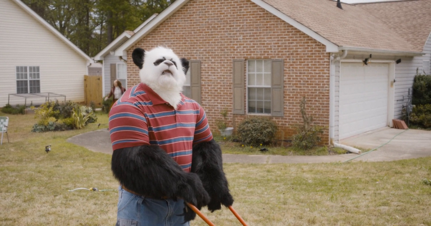 Panda humanimal mowing lawn in front of suburban home.