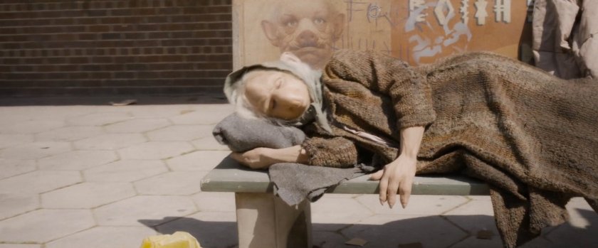 A homeless humanimal sleeping on a public bus bench.
