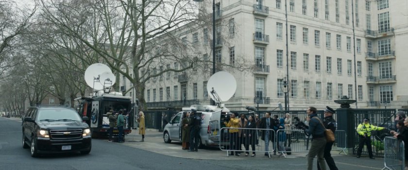 Reporters gather outside a government looking building in London as a black car approaches.