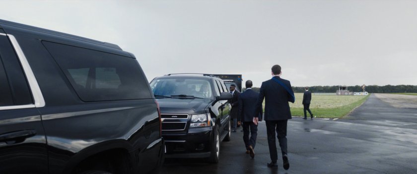 Colonel Rhodes and his team walk towards a motorcade on a tarmac.