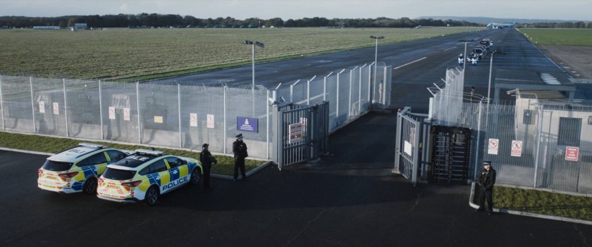 A motorcade drives through the security entrance of the airfield.