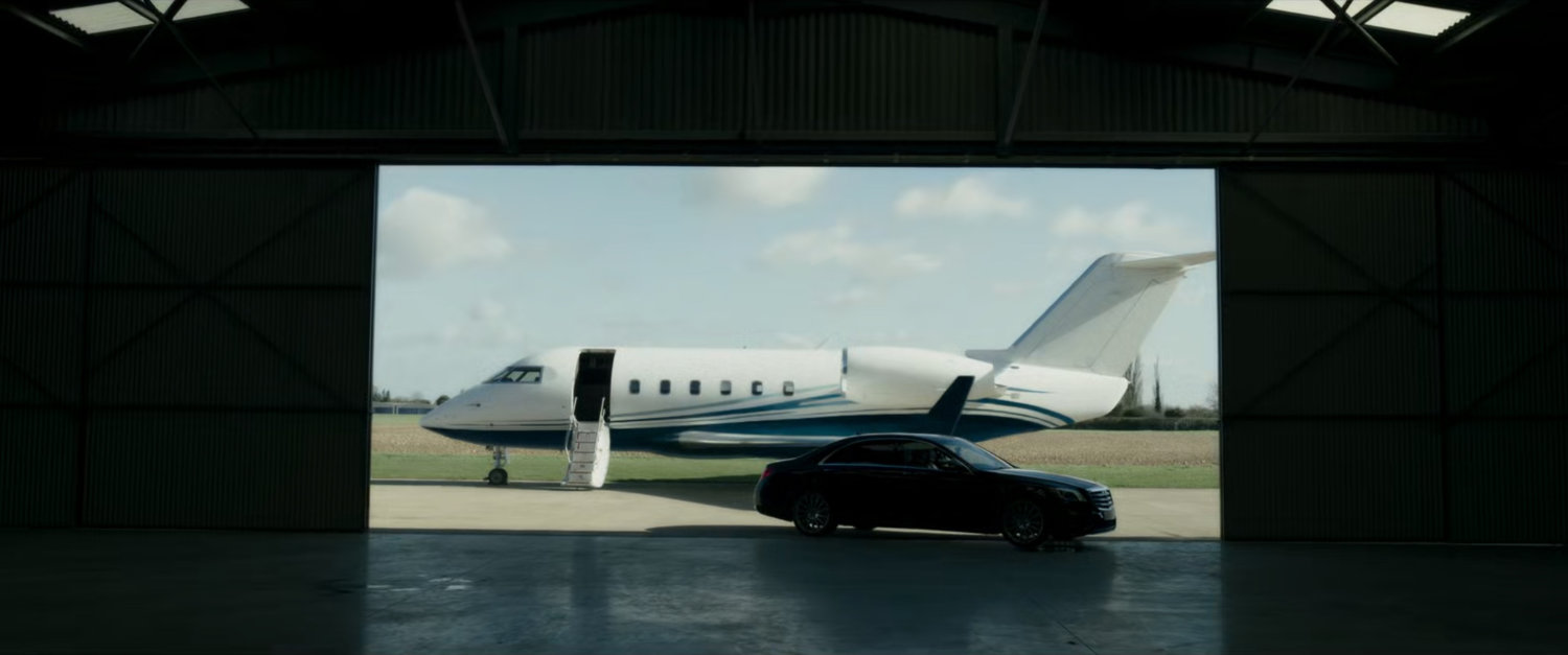 A small airplane and car framed inside aviation hangar opening.