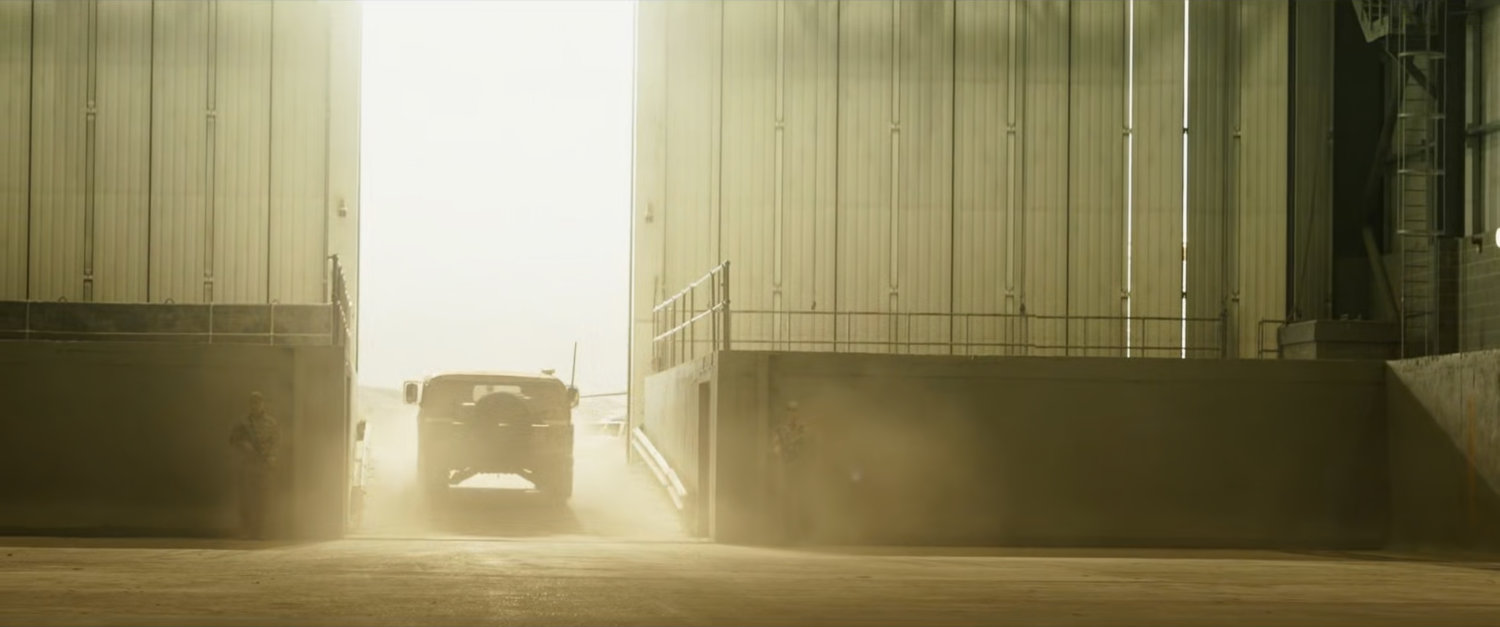 A humvee departs a desert warehouse.