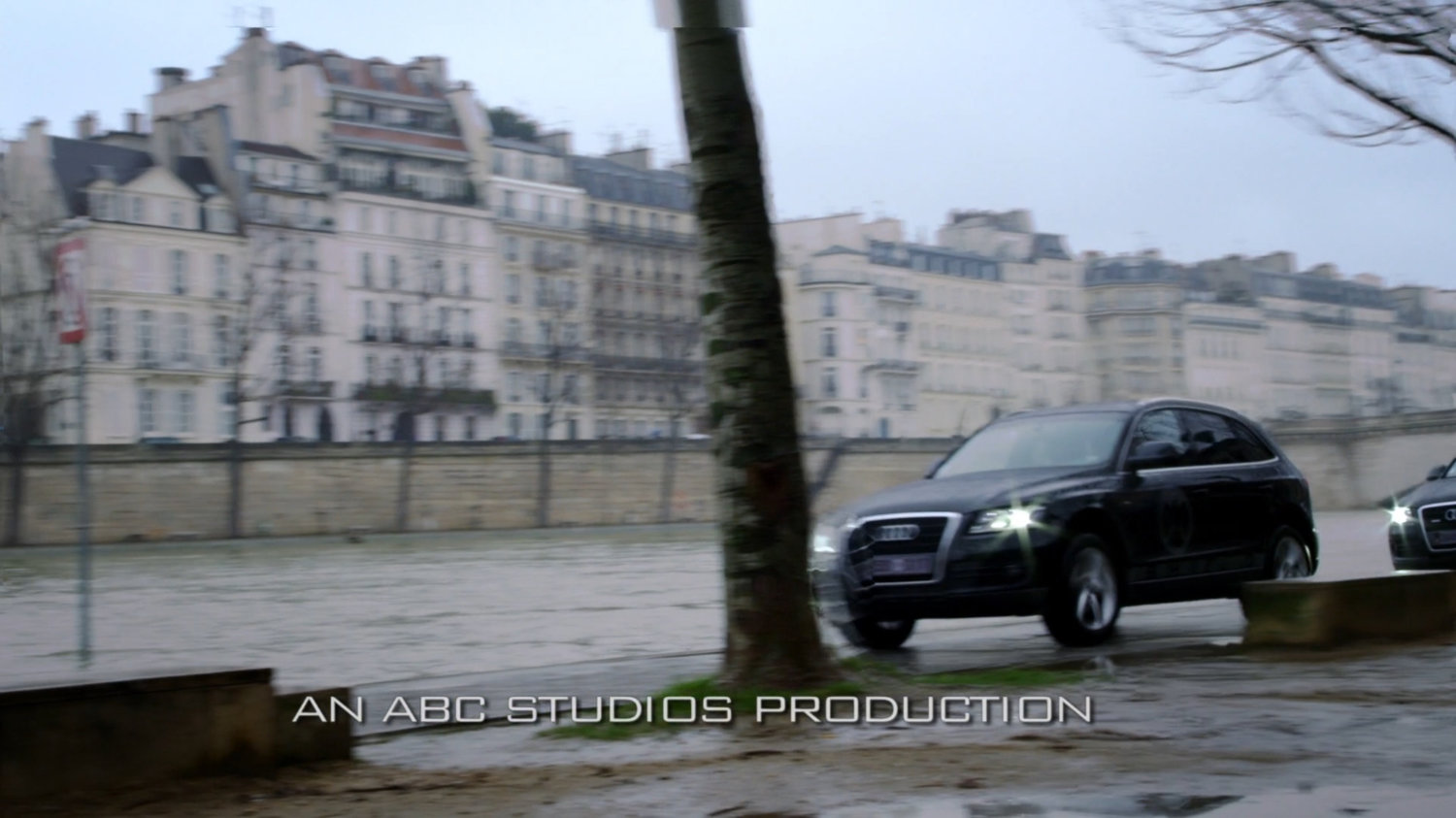 Dark cars drive along pathway next to French river. Text: An ABC Studios Production.