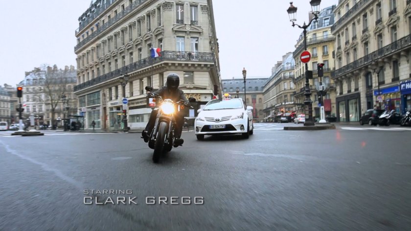 Motorcycle on Paris street. Text: Starring Clark Gregg.