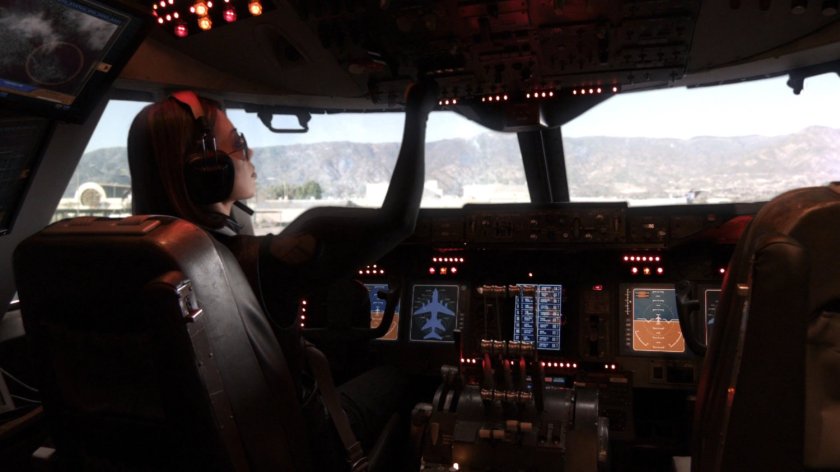 Melinda May in The Bus pilot seat, with airport outside windows.