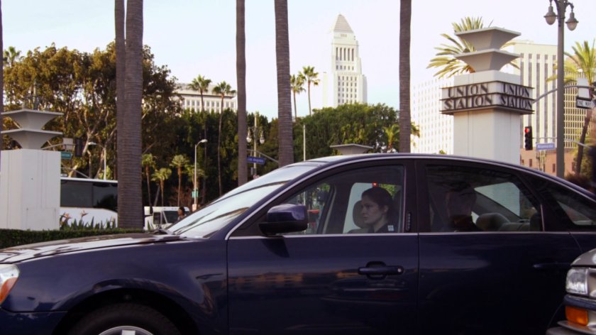 Car parked in front of Union Station with Los Angeles City Hall in background.