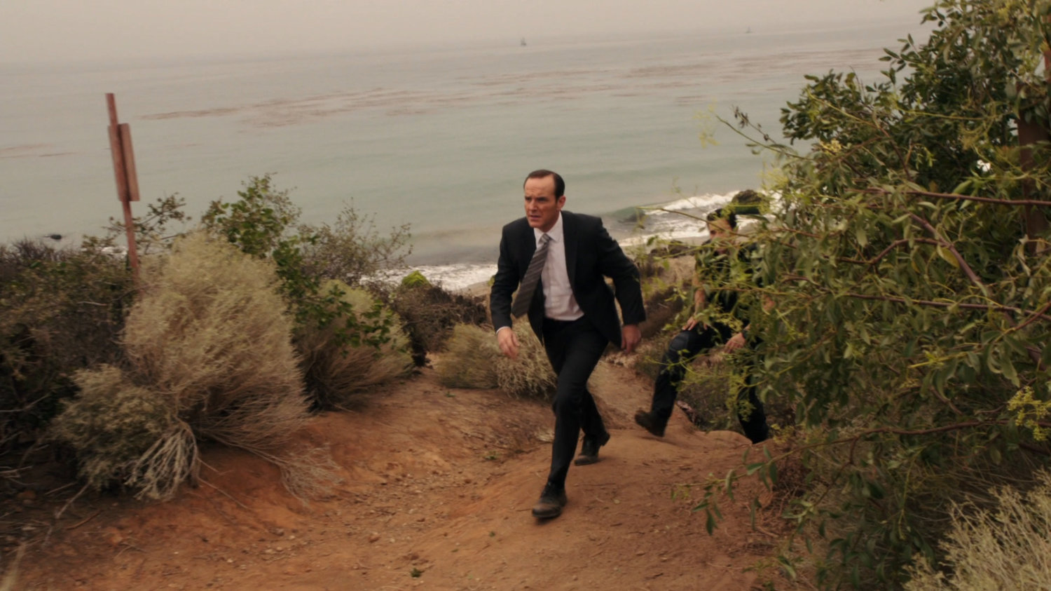 Coulson and Ward walk up path from a rocky beach.