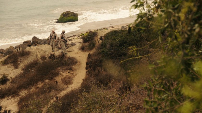 Two guards patrol a rocky beach.