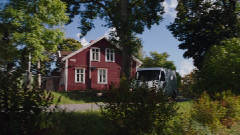A white van drives past a red house on a small country road.