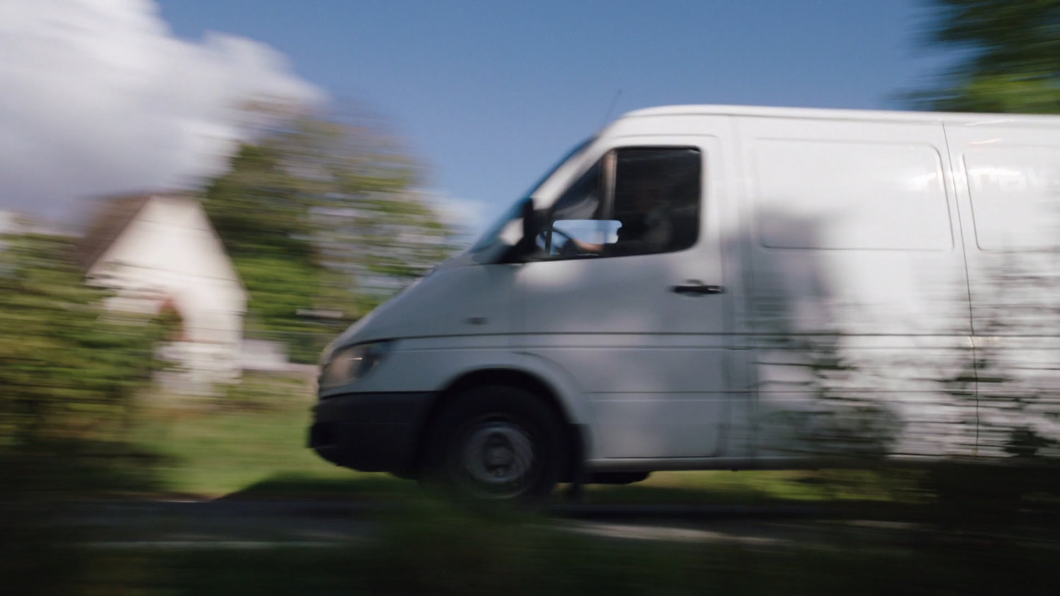 A white van speeding past camera on a small country road.