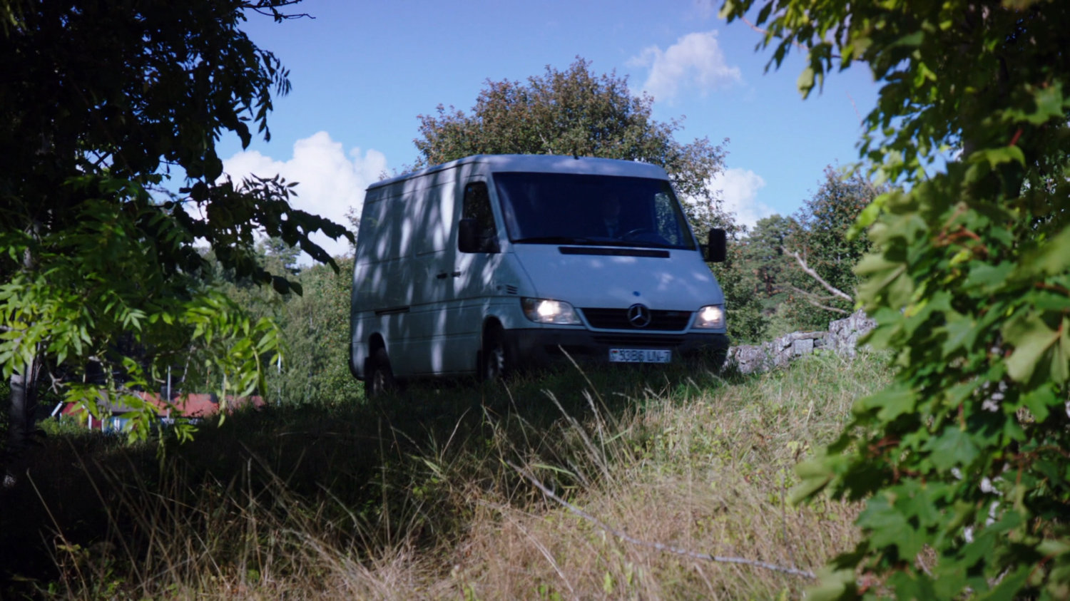 A white van drives pulls off on the side of a small country road.